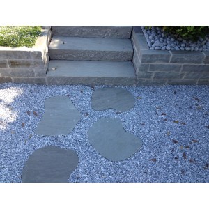 Lastre di pietra naturale come gradini in un giardino su un sentiero di ghiaia, accanto a gradini di pietra.