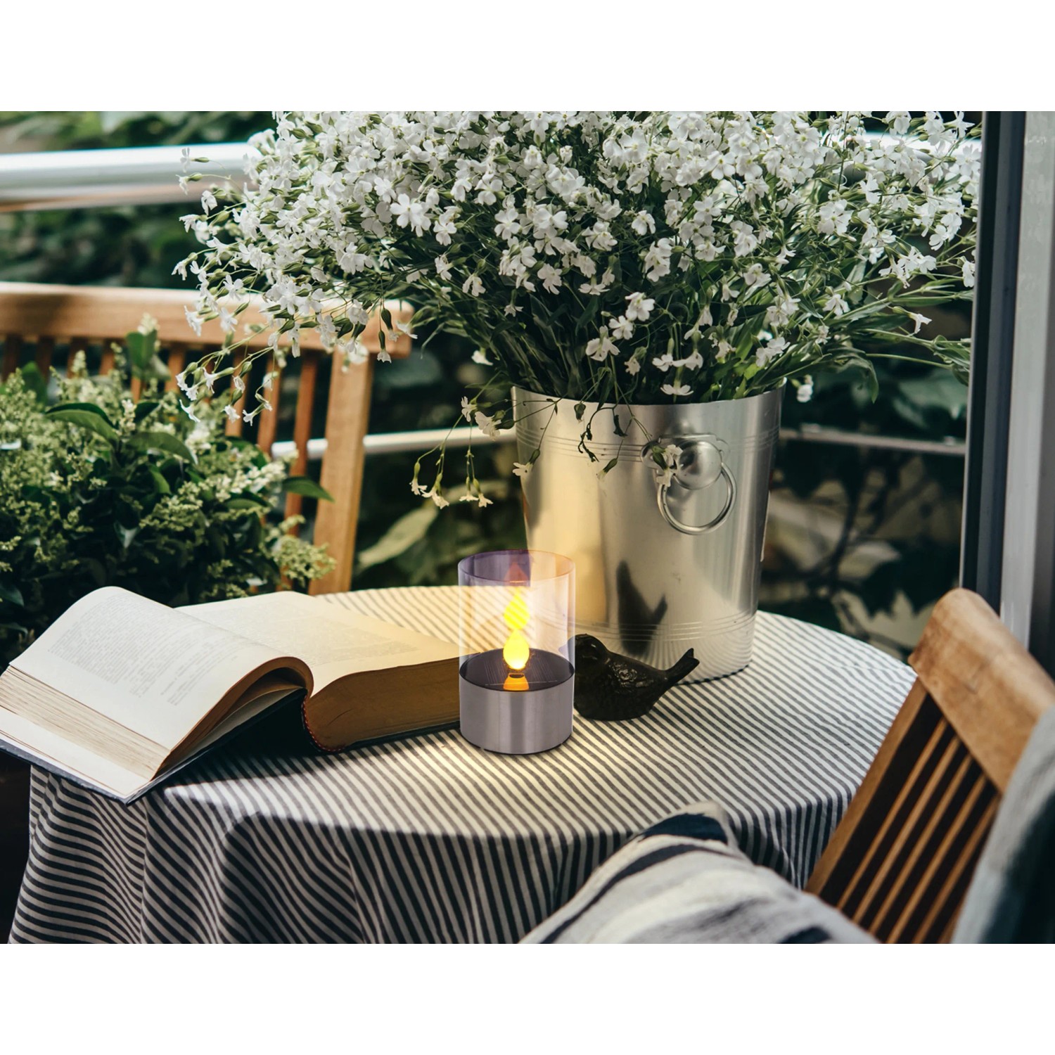Lampada da tavolo solare a LED Globo con effetto fuoco in acciaio inox su tavolo con libro e vaso di fiori.