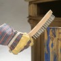Mano con guanto che utilizza spazzola metallica LUX (a 4 file) per rimuovere la ruggine dal legno.