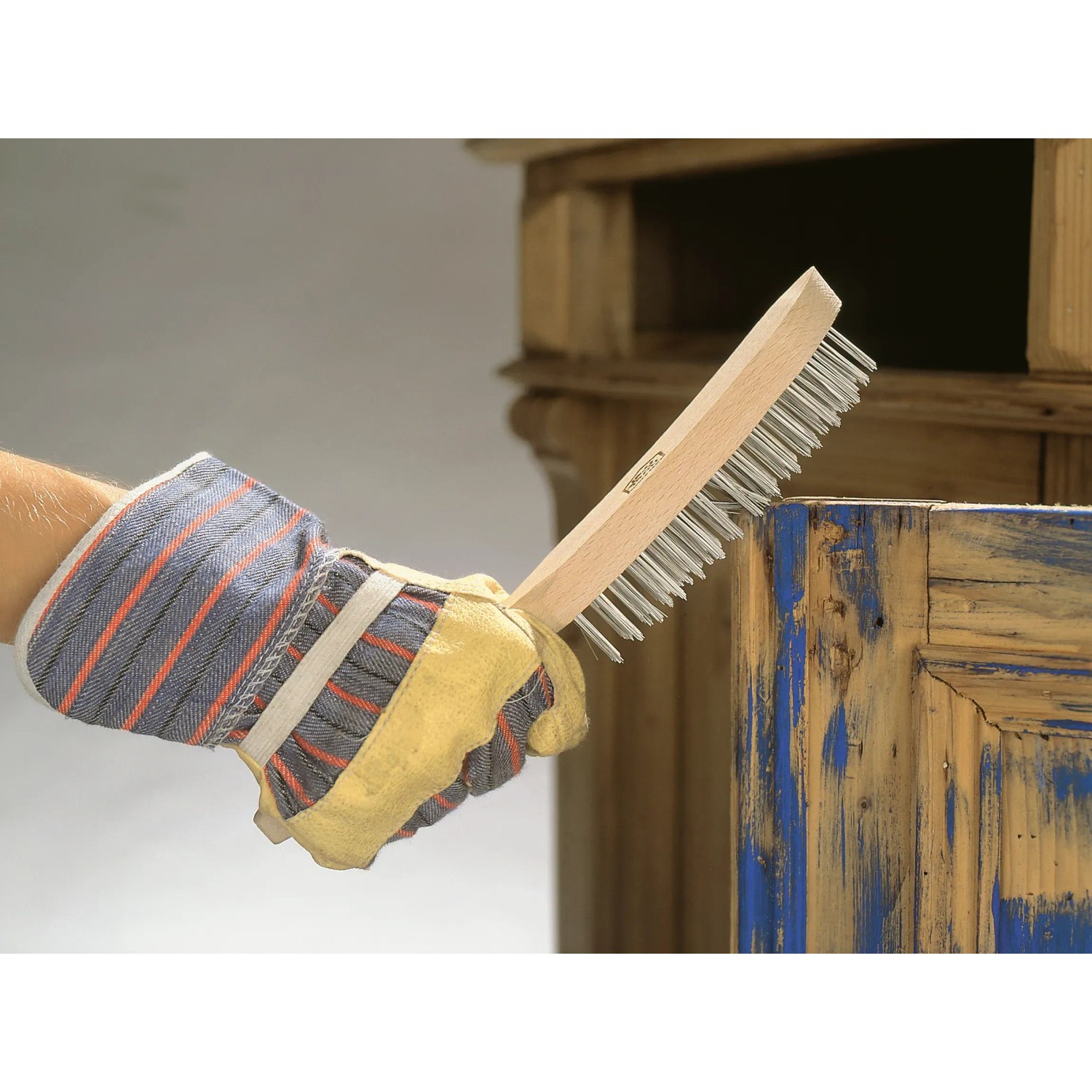 Mano con guanto che utilizza spazzola metallica LUX (a 4 file) per rimuovere la ruggine dal legno.