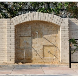 Muro decorativo in pietra con tre bocche come bordura per il giardino.