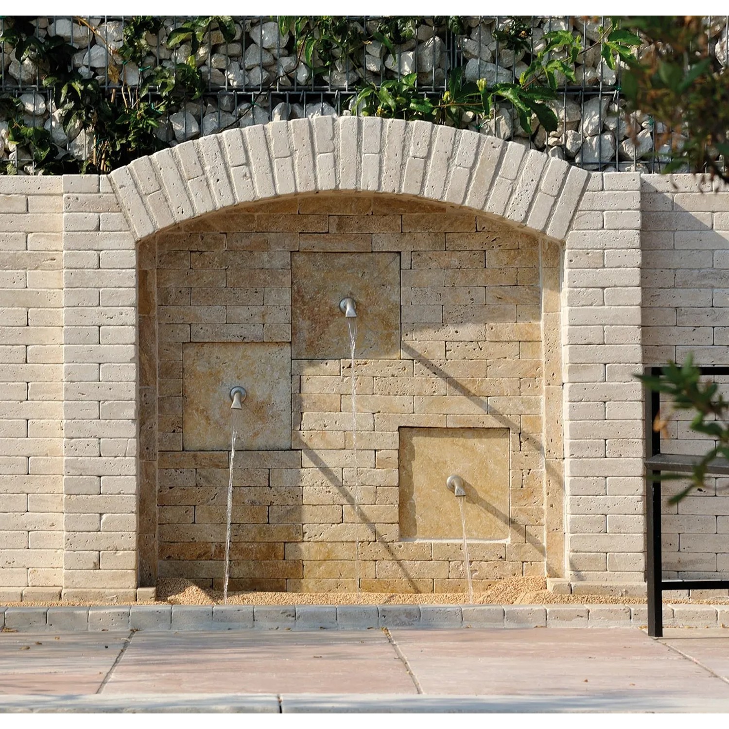 Muro decorativo in pietra con tre bocche come bordura per il giardino.