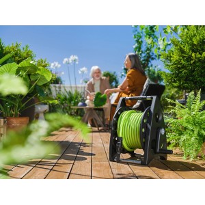 Avvolgitubo nero con tubo da giardino verde arrotolato su un patio.