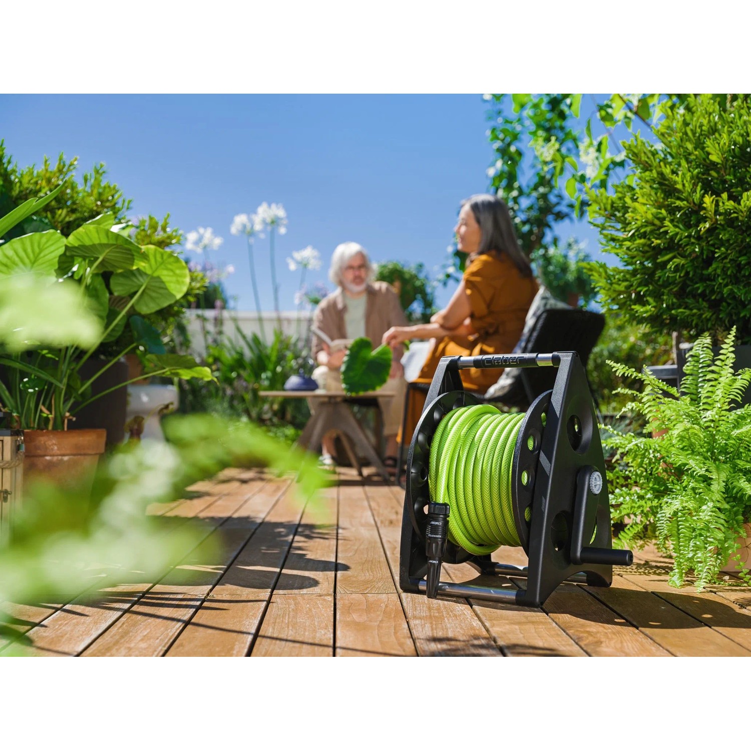 Avvolgitubo nero con tubo da giardino verde arrotolato su un patio.
